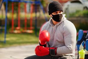 ritratto sport pugile arabo uomo in maschera medica nera boxe all'aperto durante la quarantena del coronavirus. foto