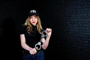 agente femminile dell'FBI in berretto e con la pistola in studio contro un muro di mattoni scuri. foto