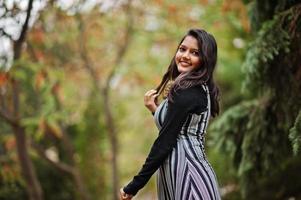 ritratto di giovane bella ragazza indiana o sud-asiatica in abito posato al parco autunnale in europa. foto