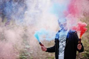 l'uomo arabo di street style con gli occhiali tiene il bagliore della mano con una bomba fumogena rossa e blu. foto