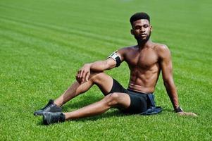 atleta maschio afroamericano sport sexy torso nudo uomo con custodia per braccio sportivo da corsa per telefono cellulare, posato sull'erba verde dello stadio di calcio. foto
