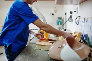 uomo protesico che realizza solette ortopediche mentre lavora in laboratorio. foto