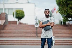 studente africano maschio posato con zaino e articoli per la scuola nel cortile dell'università, contro le bandiere di diversi paesi. foto