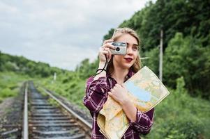 ritratto di una splendida ragazza in camicia scozzese che scatta foto con la fotocamera sulla ferrovia.