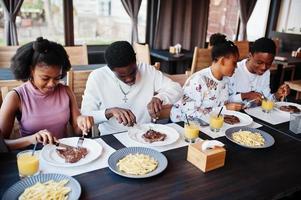 felici amici africani seduti, chiacchierando al bar e mangiando cibo. gruppo di persone di colore che si incontrano al ristorante e cenano. foto