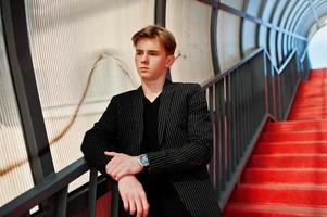 giovane ragazzo macho alla moda in giacca nera posato all'aperto di strada. incredibile modello uomo al tunnel delle scale rosse. foto