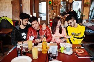 gruppo di amici asiatici seduti al caffè. felice popolo indiano che si diverte insieme, seduto sul divano e guardando i telefoni cellulari. foto