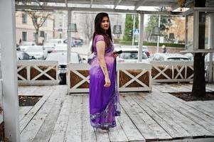 ragazza indù indiana al tradizionale saree viola poste in strada contro la terrazza in legno. foto