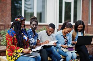 gruppo di cinque studenti universitari africani che trascorrono del tempo insieme nel campus nel cortile dell'università. amici afro neri che studiano al banco con articoli per la scuola, notebook portatili. foto