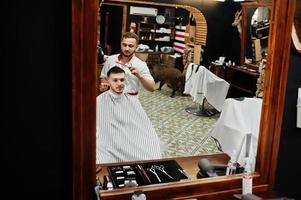 giovane uomo barbuto che si fa tagliare i capelli dal parrucchiere mentre è seduto su una sedia al barbiere. anima da barbiere. foto