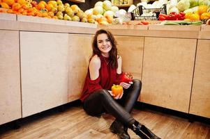 ragazza in rosso che tiene due peperoni sul negozio di frutta. foto