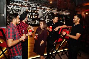 gruppo di amici indiani che si divertono e riposano al night club, bevendo cocktail vicino al bancone del bar. foto