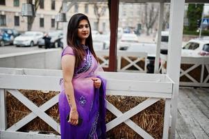 ragazza indù indiana al tradizionale saree viola poste in strada contro la terrazza in legno. foto