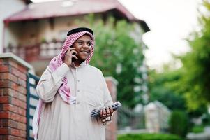 uomo d'affari arabo mediorientale posato su strada contro un edificio moderno con tablet e telefono cellulare a portata di mano. foto