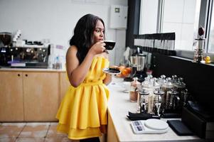 elegante donna afroamericana in abito giallo posata al caffè con una tazza di cappuccino. foto