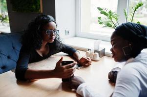 due ragazze afroamericane sedute sul tavolo al bar e guardando qualcosa sul telefono cellulare. foto