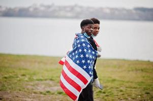 due adolescenti africani amici con bandiera americana al parco che indossano maschere mediche proteggono da infezioni e malattie quarantena del virus del coronavirus. foto