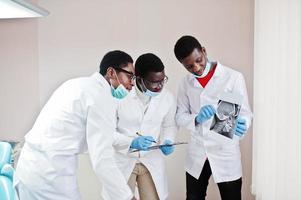 tre medici maschi afroamericani che lavorano, discutono con i colleghi in clinica e indicano il cranio a raggi X. foto