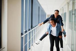 due amiche africane in giacca di jeans divertendosi, sono saltate sulle spalle insieme al coperto. foto