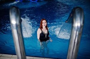 ragazza dai capelli rossi sexy in costume da bagno nero che riposa nella piscina del parco acquatico. foto