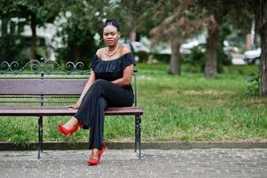 ragazza africana in posa per strada di città indossa su nero, seduta sulla panchina. foto