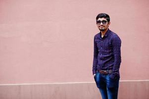 giovane indiano su camicia e occhiali da sole in posa contro il muro rosa. foto