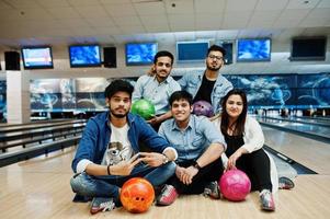 gruppo di cinque popoli dell'Asia meridionale che si riposano e si divertono al bowling club, seduti su una pista da bowling con le palle sulle mani. foto