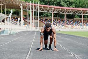 atleta maschio afroamericano in abbigliamento sportivo che corre da solo lungo una pista da corsa allo stadio. foto