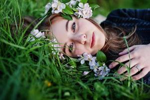 giovane ragazza bruna sdraiata sull'erba verde con rami di albero in fiore. foto