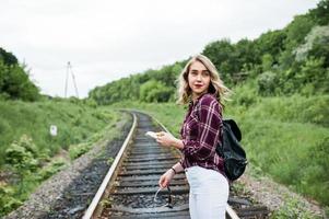 ritratto di una bella ragazza bionda in camicia scozzese che cammina sulla ferrovia con la mappa nelle sue mani. foto