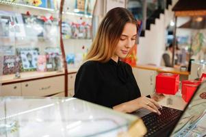 ritratto di giovane donna caucasica venditore utilizzando laptop. piccola impresa di negozio di souvenir di caramelle. foto