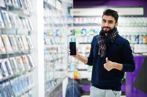 l'acquirente del cliente dell'uomo della barba indiana presso il negozio di telefoni cellulari sceglie il suo nuovo smartphone e mostra il pollice in su. concetto di popoli e tecnologie dell'Asia meridionale. negozio di cellulari. foto