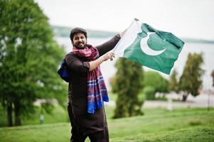 l'uomo pakistano indossa abiti tradizionali e tiene la bandiera del pakistan. foto