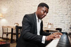 forte e potente uomo afroamericano in abito nero suona il pianoforte. foto