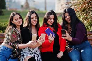 un gruppo di quattro ragazze latine felici e graziose dell'Ecuador in posa in strada e guardando i telefoni cellulari. foto