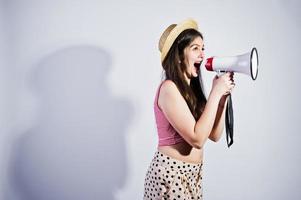 ritratto di una splendida ragazza in costume da bagno e cappello parla nel megafono in studio. foto