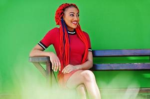 ragazza afroamericana carina e snella in abito rosso con dreadlocks poste sul muro verde del fondo del banco. modello nero elegante. foto