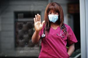 medico femminile afroamericano in uniforme di laboratorio rossa in maschera facciale protettiva. concetto di medicina, professione e assistenza sanitaria. fermare l'infezione da coronavirus. foto