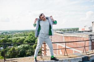 sognatore elegante uomo macho in abito grigio, cappello e occhiali in posa sul tetto. foto