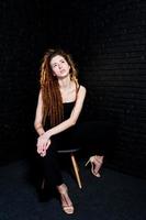 riprese in studio di una ragazza in nero su una sedia con dreadlocks su sfondo di mattoni. foto