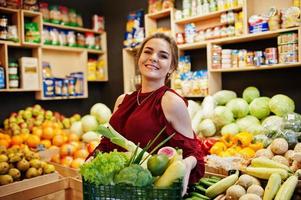 ragazza in rosso che tiene diverse verdure sul negozio di frutta. foto