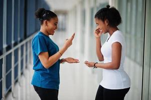 due amiche africane in t-shirt giocano insieme a forbici di carta sasso al coperto. foto