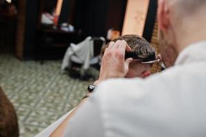 giovane uomo barbuto che si fa tagliare i capelli dal parrucchiere mentre è seduto su una sedia al barbiere. anima da barbiere. foto