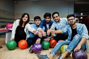 gruppo di cinque popoli dell'Asia meridionale che si riposano e si divertono al bowling club. tenendo le palle da bowling, seduto sul vicolo e mostrare il pollice in su le mani. foto