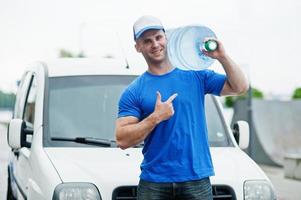 uomo delle consegne davanti al furgone che consegna bottiglie d'acqua che mostrano il dito. foto