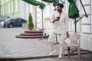 elegante uomo afro in abito beige vecchia scuola con telefono cellulare. giovane maschio africano alla moda in giacca casual sul torso nudo. foto