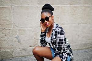 ragazza afroamericana hip hop su occhiali da sole e pantaloncini di jeans. ritratto di moda di strada casual di donna nera. foto