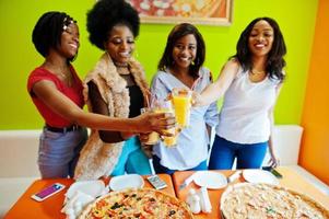 quattro giovani ragazze africane in un ristorante pizzeria dai colori vivaci che tintinnano succhi di frutta. foto