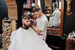 giovane uomo barbuto che si fa tagliare i capelli dal parrucchiere mentre è seduto su una sedia al barbiere. anima da barbiere. foto