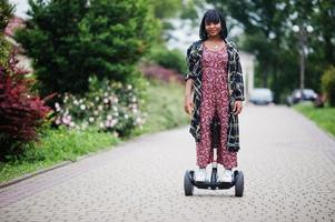 bella donna afroamericana utilizzando segway o hoverboard. ragazza nera su scooter elettrico autobilanciante a doppia ruota. foto